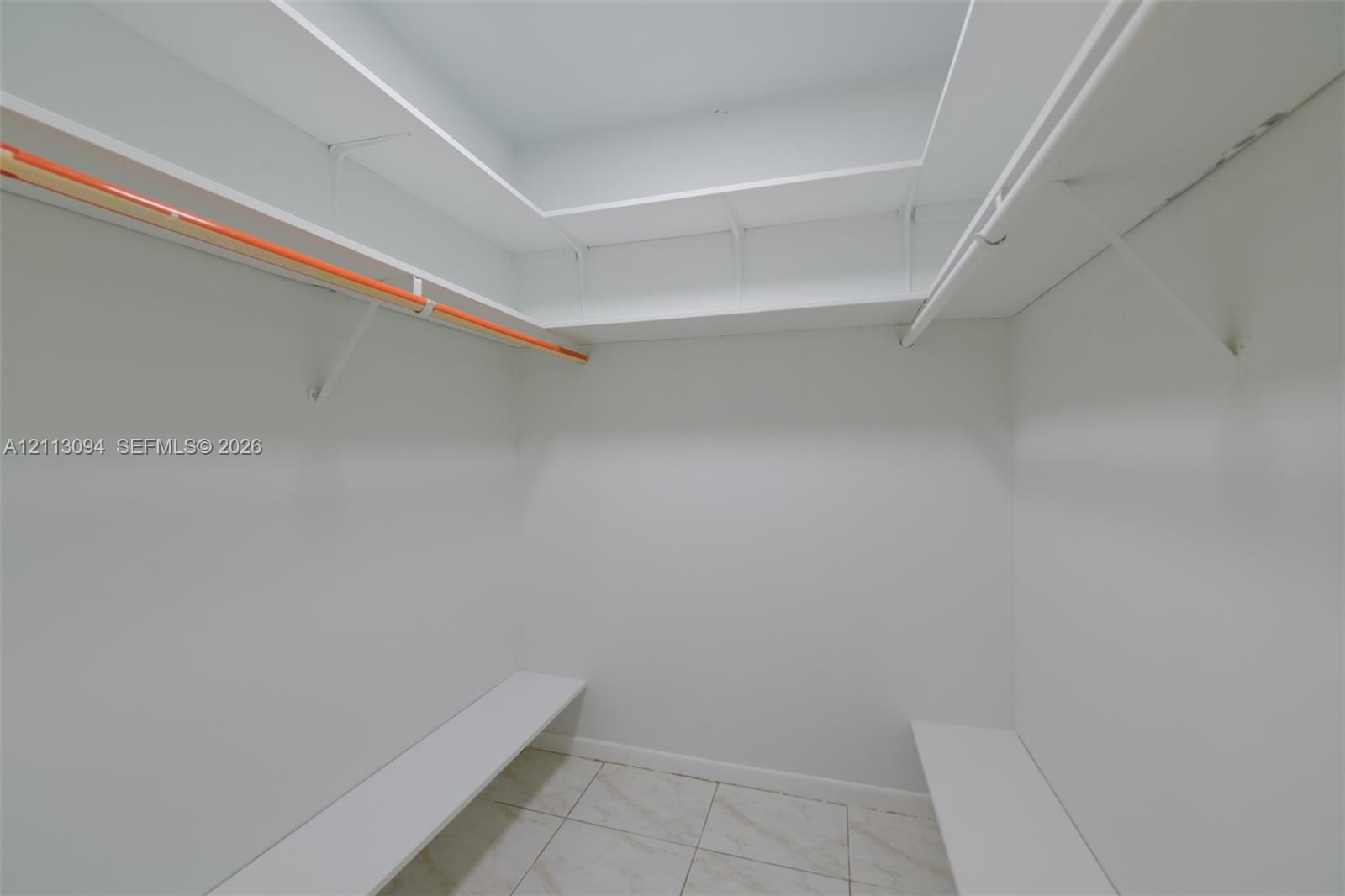 Walk-in storage space featuring custom multi-level shelving, integrated hanging rods, and tile flooring