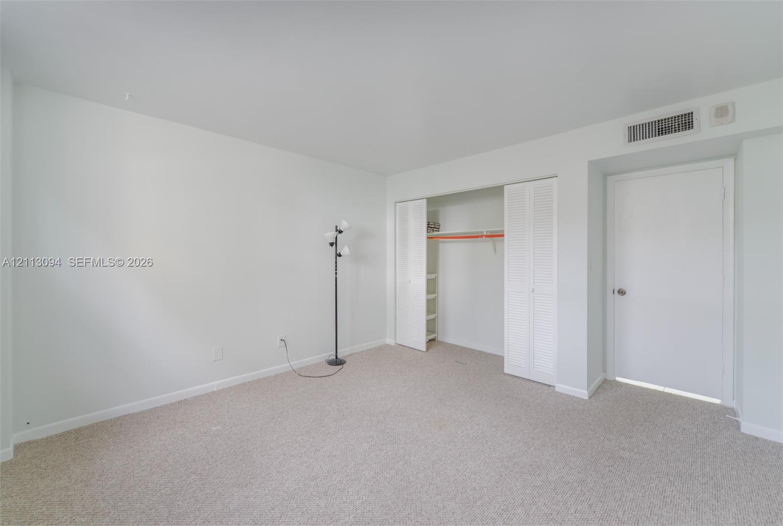 Neutral-toned carpeting, white walls, and a closet with bifold louvered doors