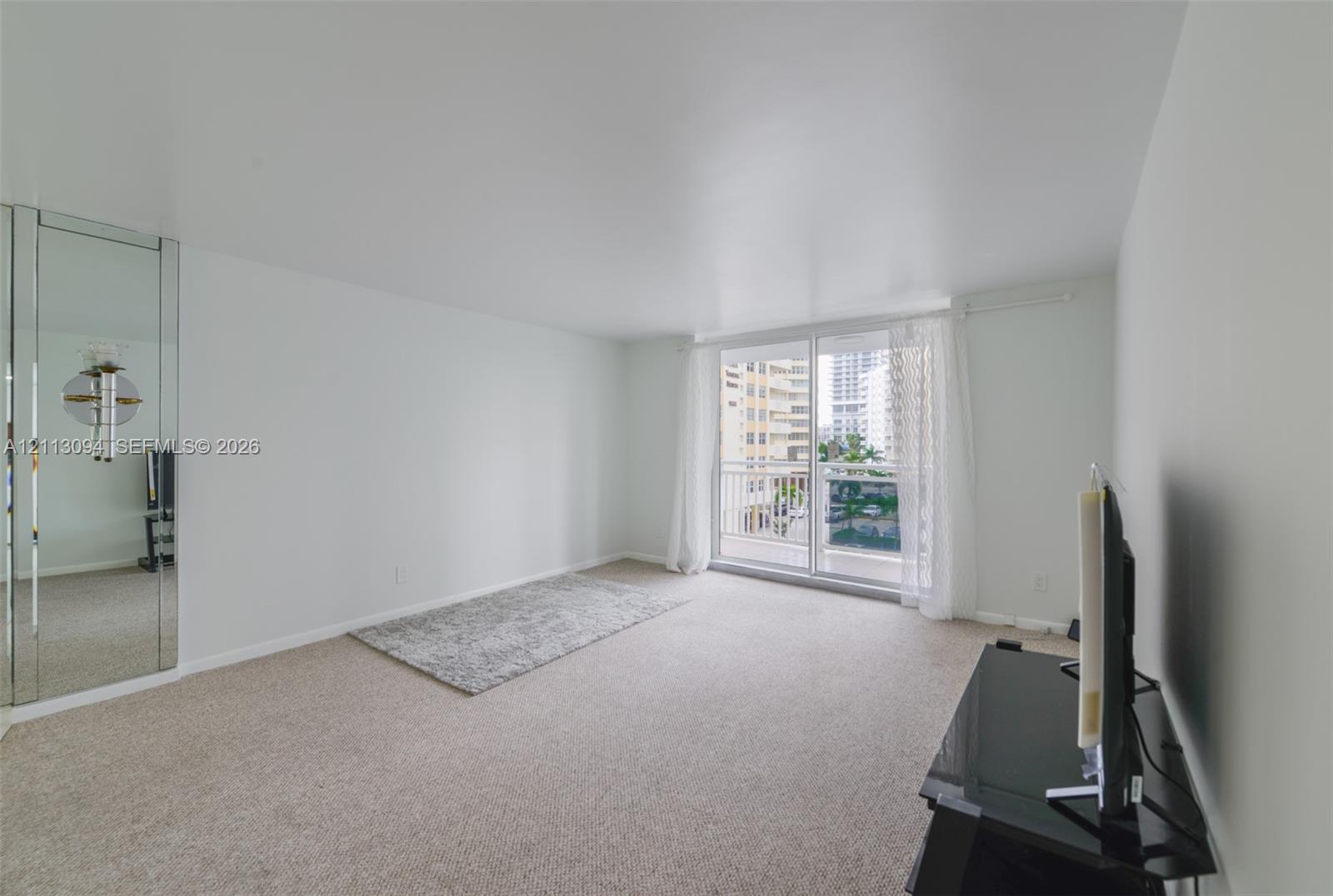Living area featuring wall-to-wall carpeting, floor-to-ceiling mirrored wall panels, and a sliding glass door providing access to a private balcony