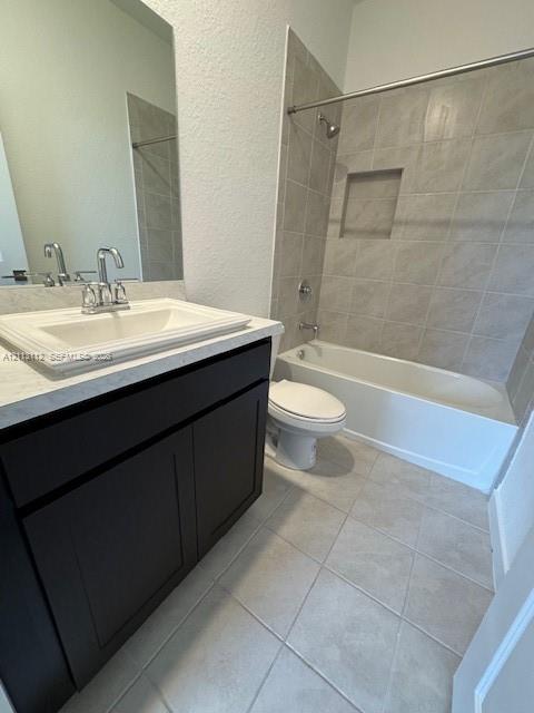 Bathroom featuring a dark wood-finish vanity, light stone-composite countertop with integrated sink, porcelain tile flooring, and a tiled tub-shower combination with a built-in recessed niche
