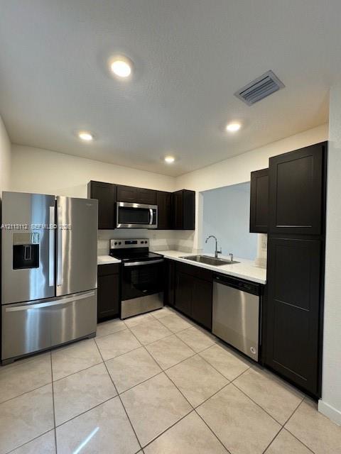 Kitchen featuring dark-finish cabinetry, solid-surface countertops, stainless steel appliances, and tile flooring