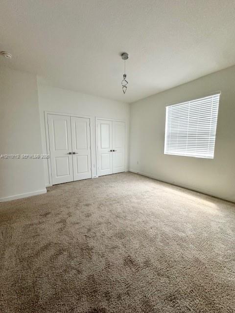 Interior space featuring neutral-toned carpeting, two sets of panel doors with metallic hardware, a single geometric pendant light fixture, and a window with horizontal blinds