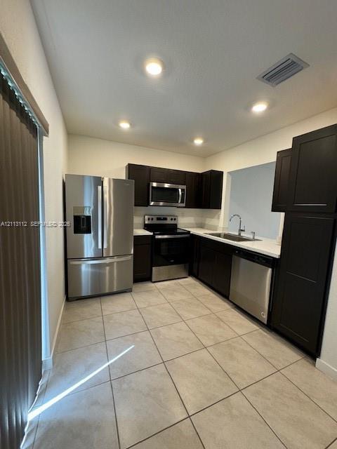 Kitchen featuring dark cabinetry, stainless steel appliances, solid-surface countertops, and ceramic tile flooring Kitchen featuring dark cabinetry, stainless steel appliances, solid-surface countertops, and ceramic tile flooring