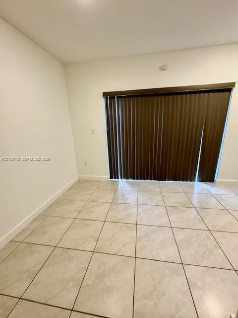 Neutral-toned tile flooring and full-height sliding glass doors featuring vertical blinds