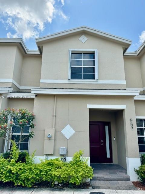 Exterior featuring a stucco facade, dark-toned entry door with a vertical glass panel, gabled roofline, decorative diamond-shaped wall accents, and paved entry path