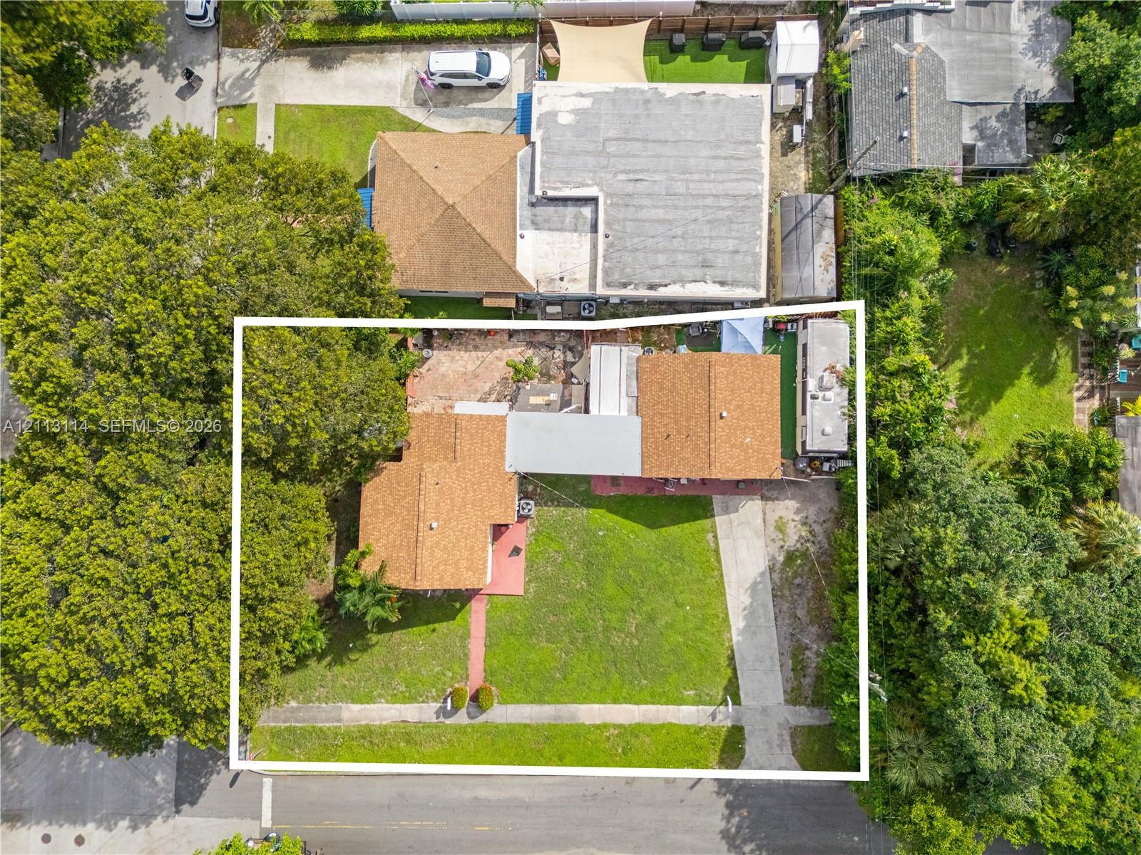Aerial perspective featuring low-rise structures with shingle roofing, concrete driveway, and expansive lawn area with mature trees