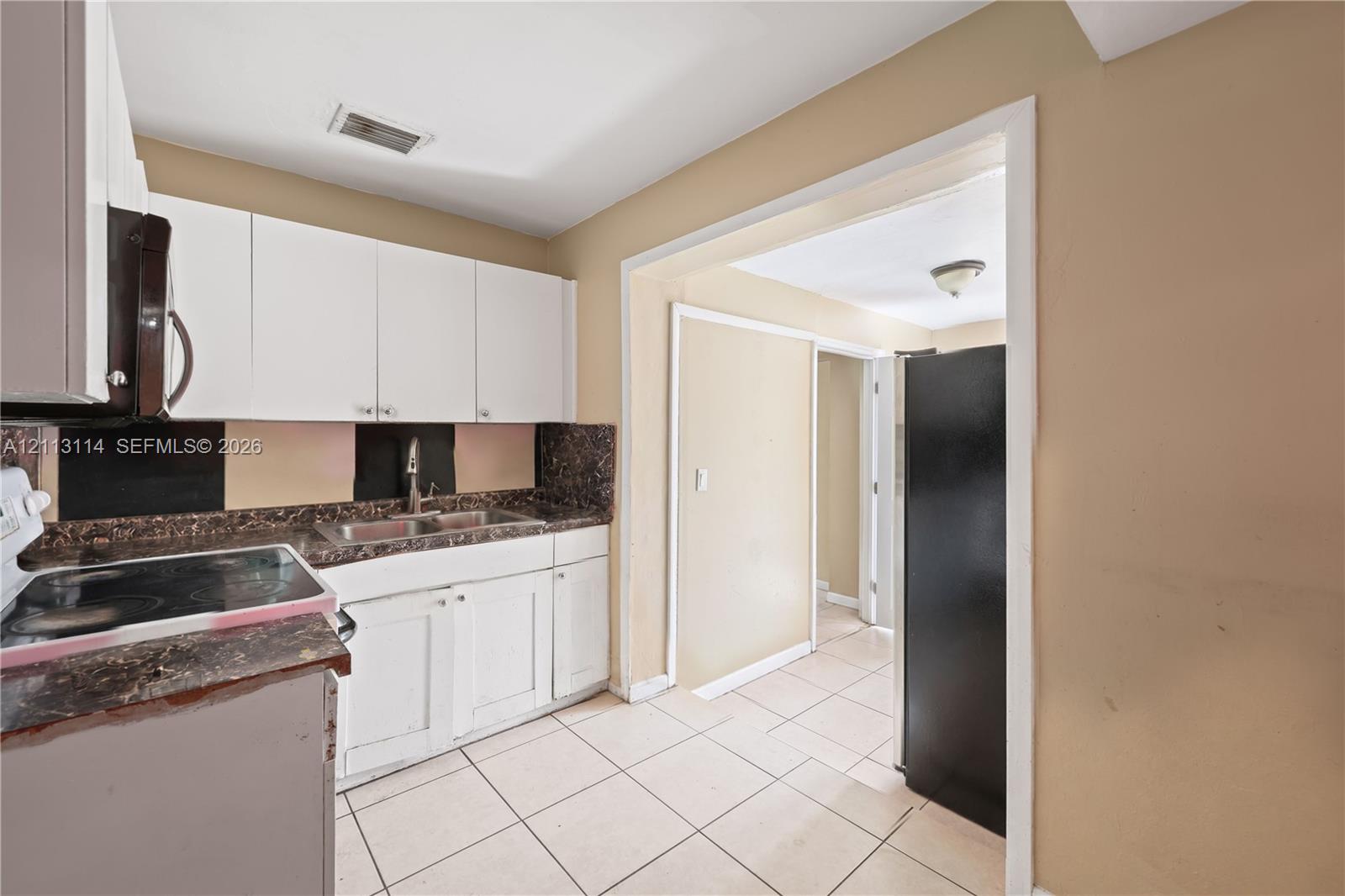 Kitchen featuring white cabinetry, stone-finish countertops, tile flooring, and a double-basin stainless steel sink