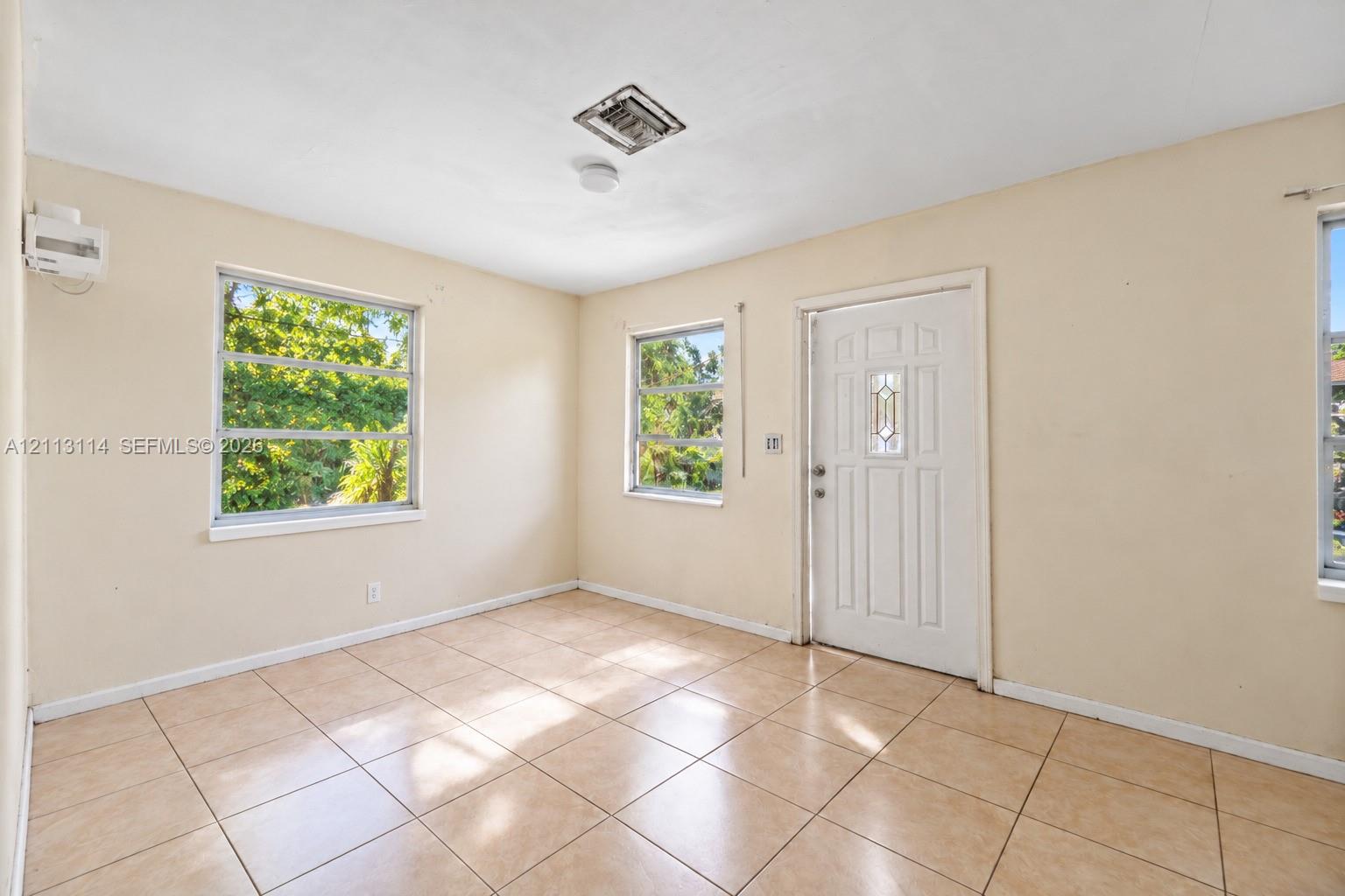 Interior space featuring neutral wall tones, ceramic tile flooring, multiple windows, and a glass-inlay entry door