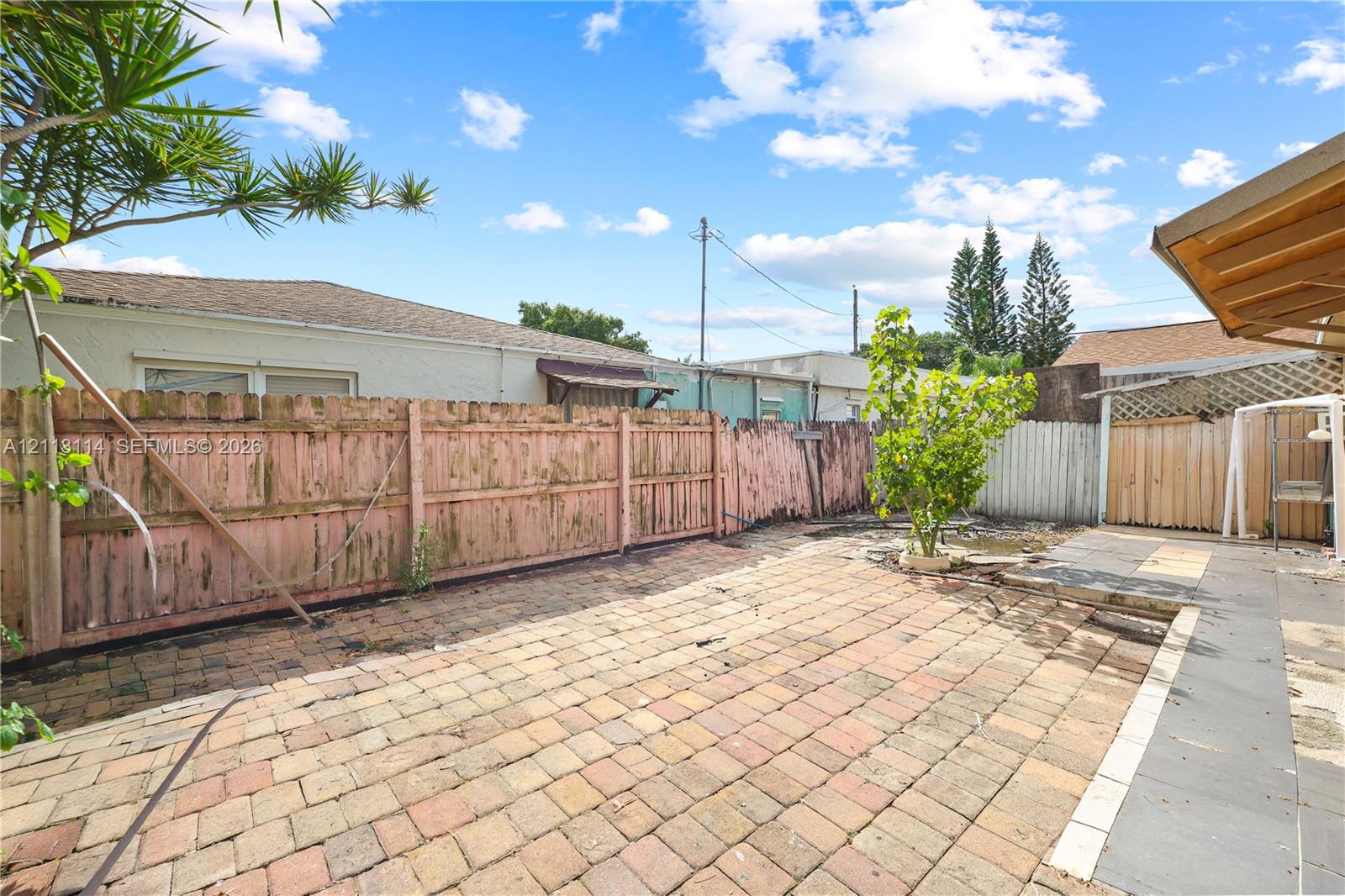 Rear courtyard featuring a brick-paved patio, wooden perimeter fencing, and an overhead patio cover