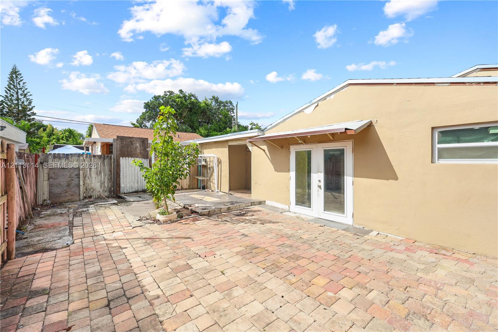 Exterior space featuring a paved brick patio, French doors with an attached metal awning, and wood-panel fencing