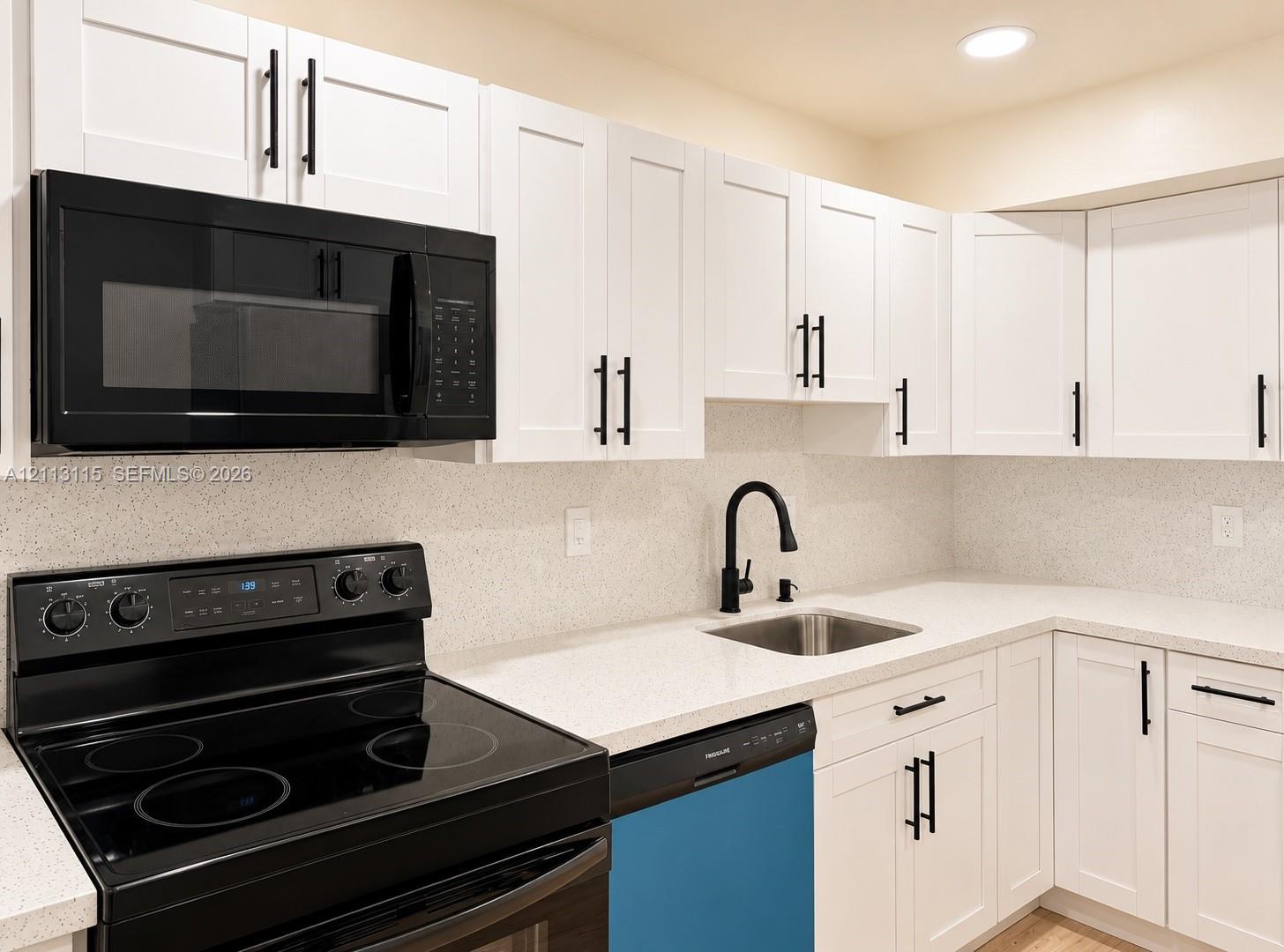 Kitchen featuring white shaker-style cabinetry, solid-surface countertops, black finish hardware, a stainless steel undermount sink with a matte black faucet, and a black appliance suite
