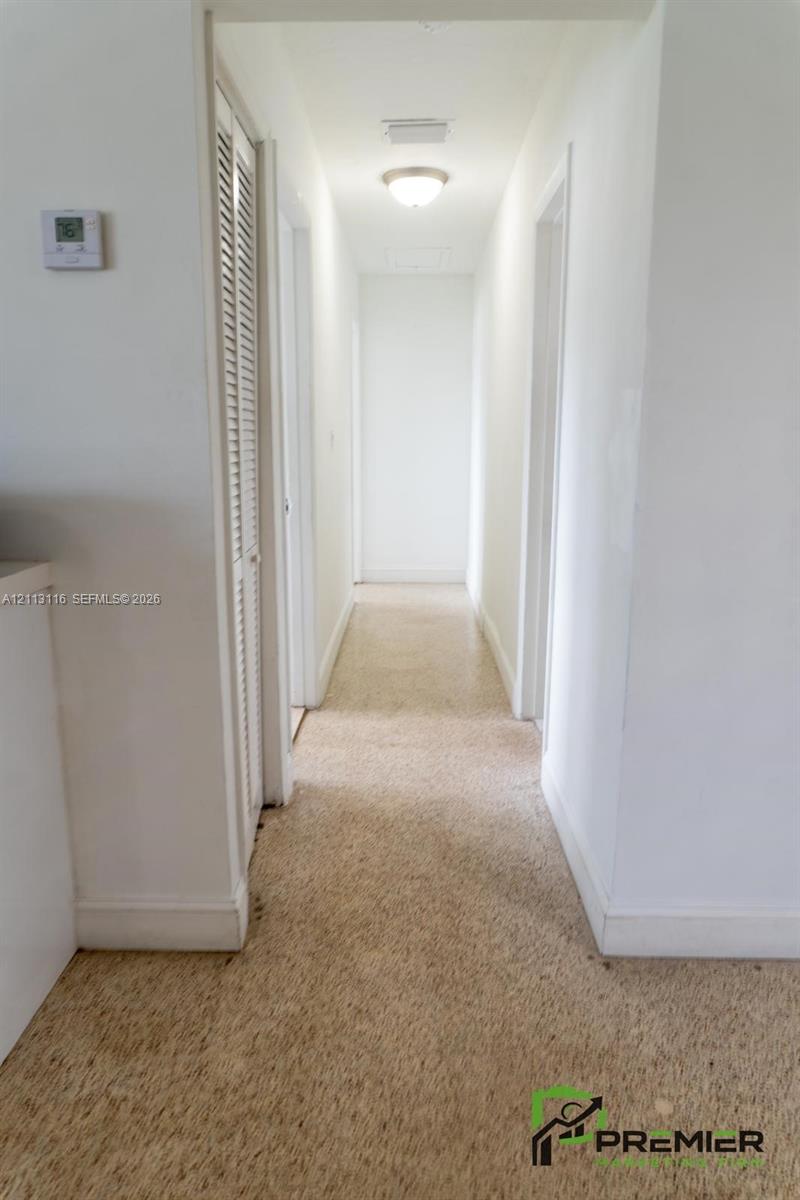 Hallway featuring neutral-toned carpeting, louvered closet doors, and a ceiling-mounted flush mount light fixture