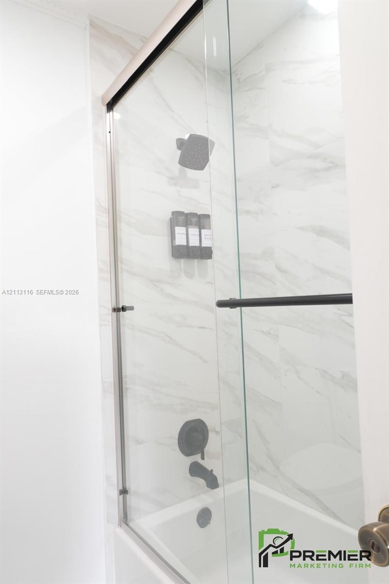 Shower enclosure featuring large-format tile surround, glass sliding door, and matte black shower fixtures