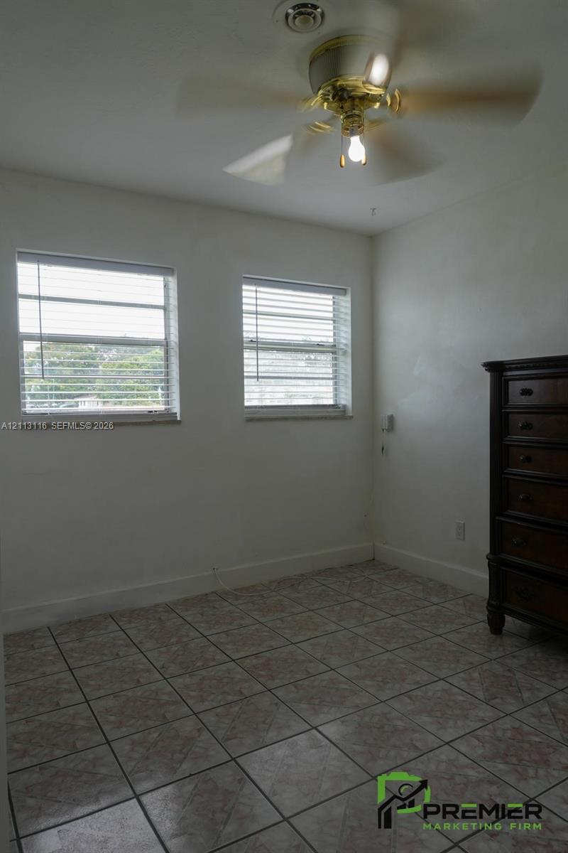 Room featuring tile flooring, dual windows with horizontal blinds, and a ceiling fan