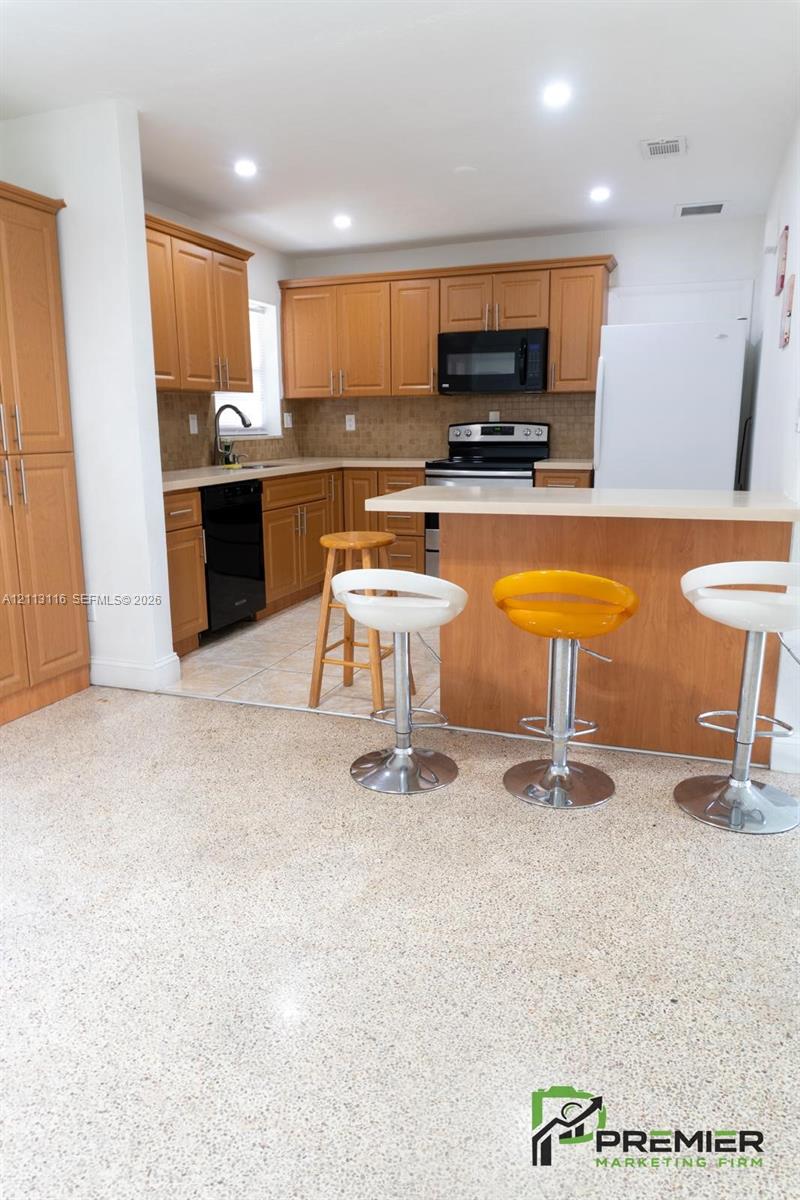 Kitchen featuring medium-tone wood cabinetry, solid-surface countertops, tile flooring, and a breakfast bar
