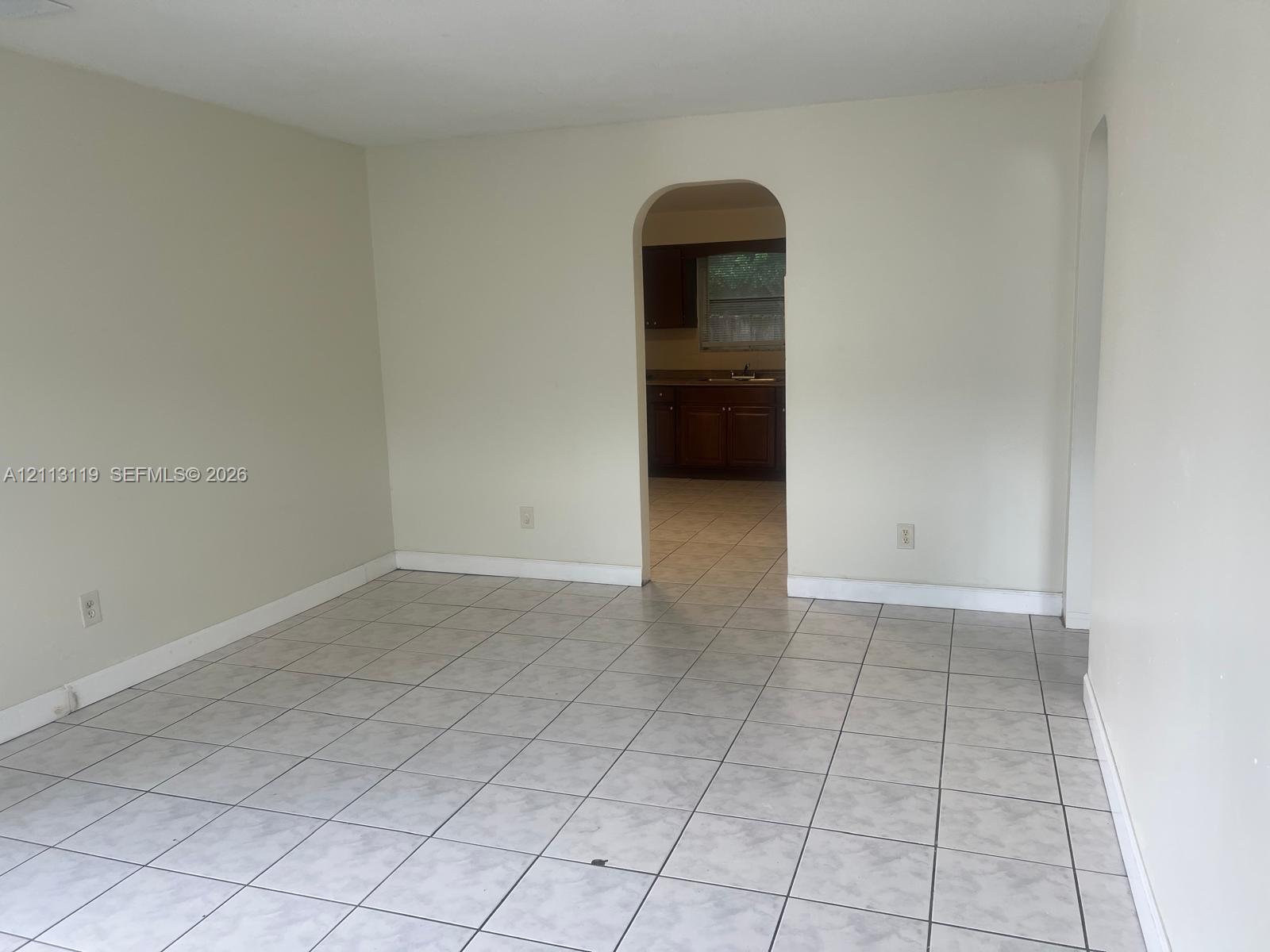 Neutral-toned interior featuring large-format ceramic tile flooring, an arched doorway, and white wall finishes