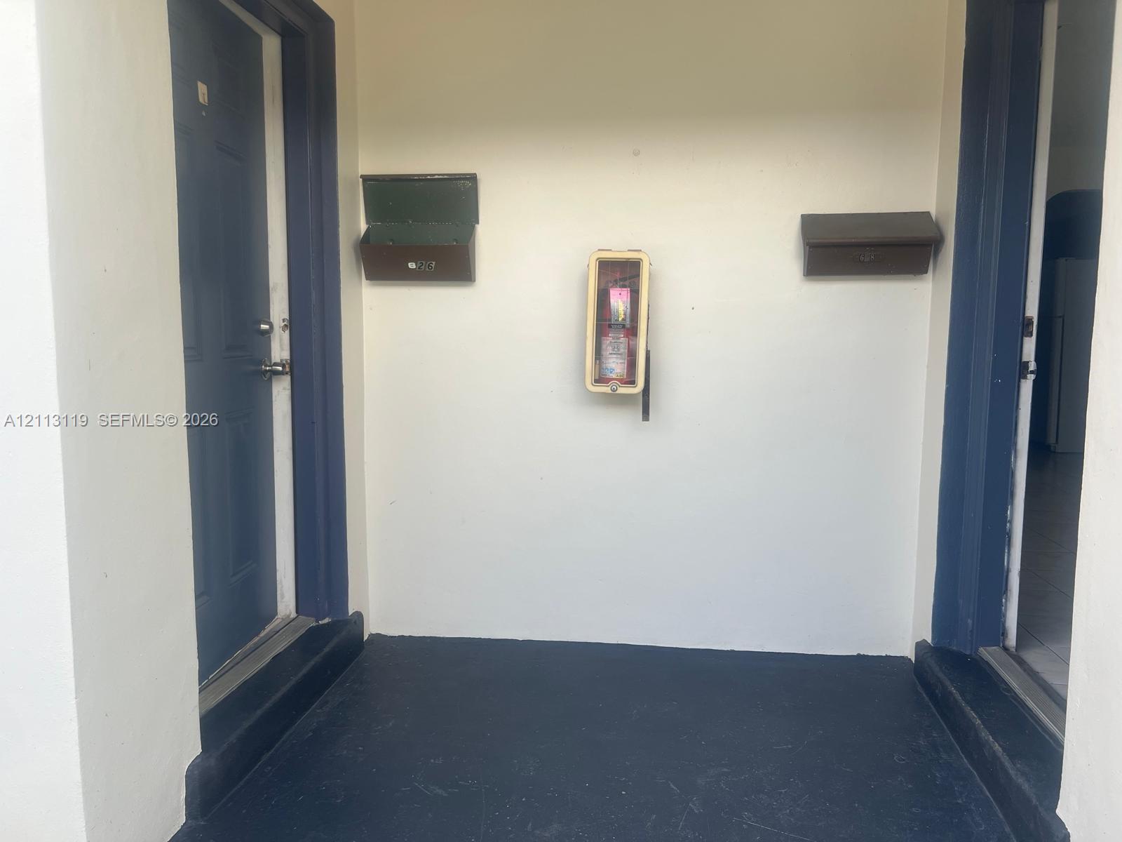 Exterior entrance featuring dual entryways with dark-toned door frames, two wall-mounted mailboxes, and a central fire extinguisher cabinet