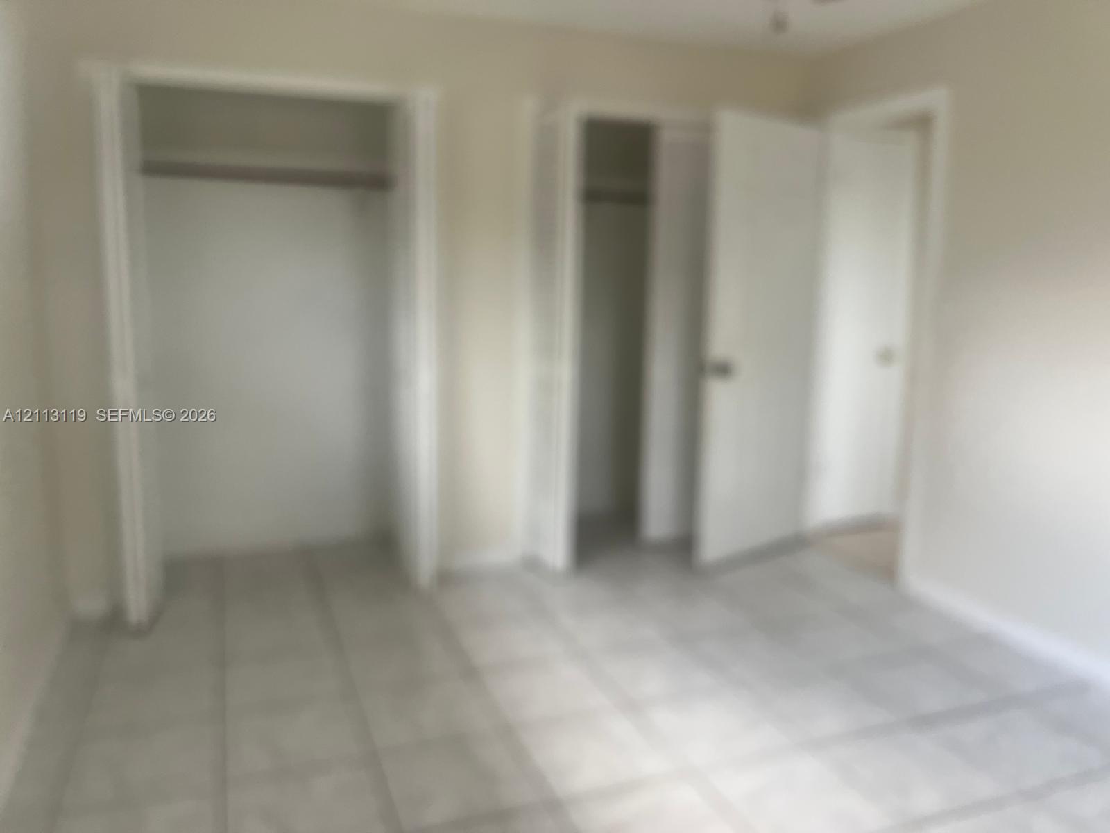 Interior space featuring neutral wall paint, tile flooring, and dual reach-in closets with hinged doors