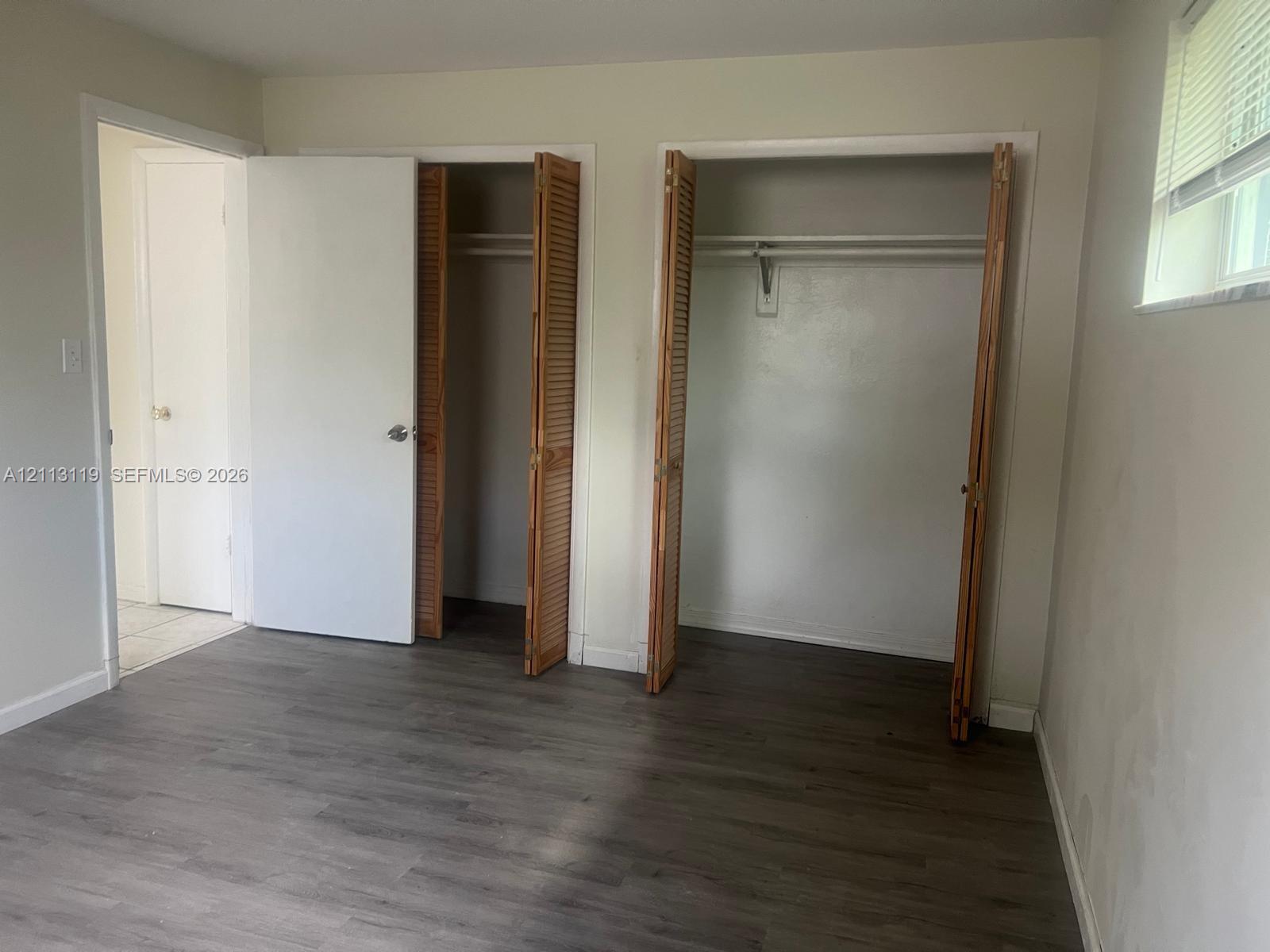 Room featuring wood-finish flooring, two dual-door closets with louvered panels, and a built-in hanging rod