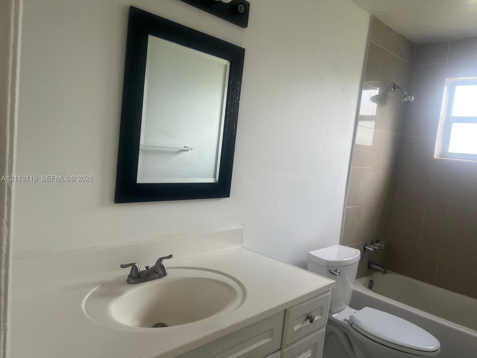 Bathroom featuring a white vanity with an integrated sink, framed wall mirror, light-colored tile shower surround, and a double-handle faucet fixture