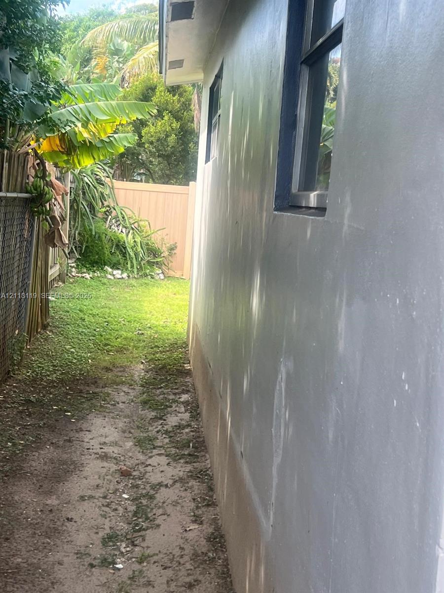 Exterior wall featuring smooth stucco finish, dark-framed windows, and a fenced side yard with mature vegetation