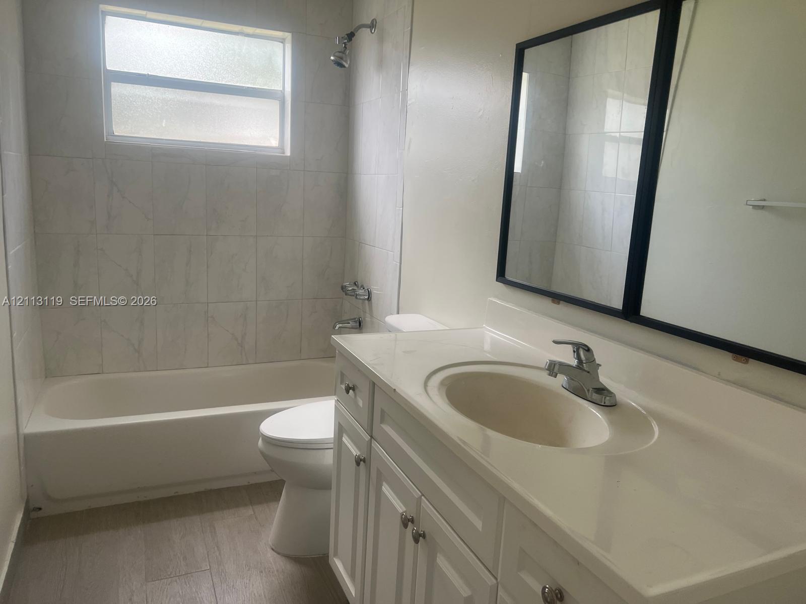 Bathroom featuring a vanity with integrated sink, porcelain tile shower surround, wood-finish flooring, and a framed wall mirror