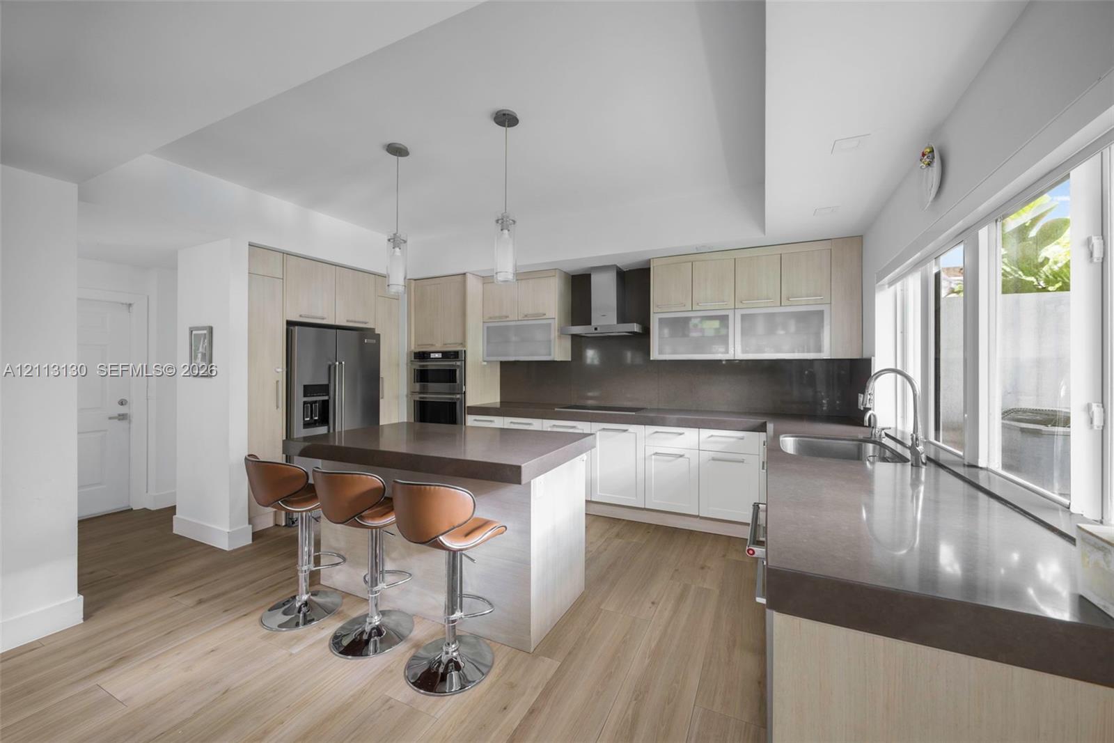Kitchen featuring wood-finish cabinetry, stone countertops, stainless steel appliances, double wall ovens, and dual pendant lighting