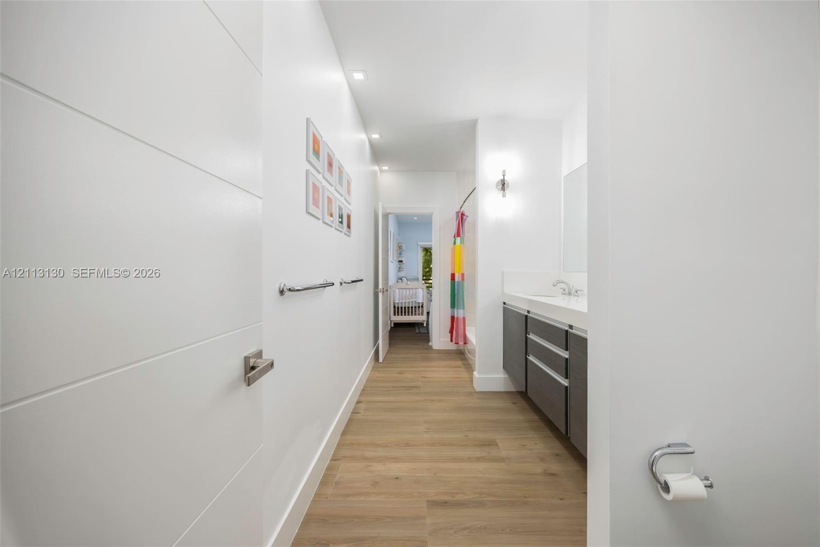 Bathroom featuring wood-finish flooring, a floating vanity with a light-toned countertop, integrated dual-basin sink, recessed lighting, and wall-mounted vanity sconces