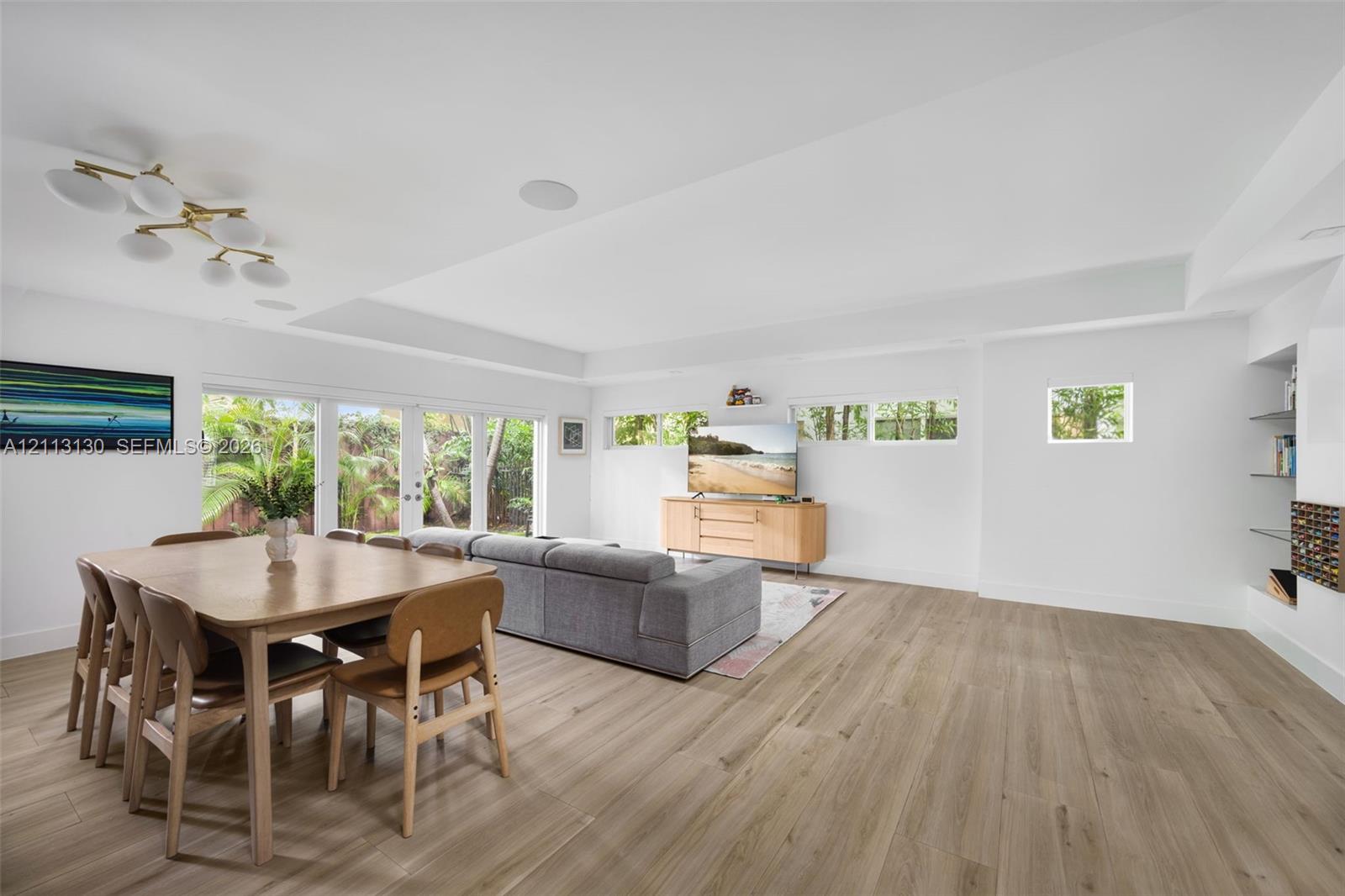 Open-concept interior featuring wood-finish flooring, recessed lighting, multi-panel glass exterior doors, clerestory windows, and built-in glass shelving