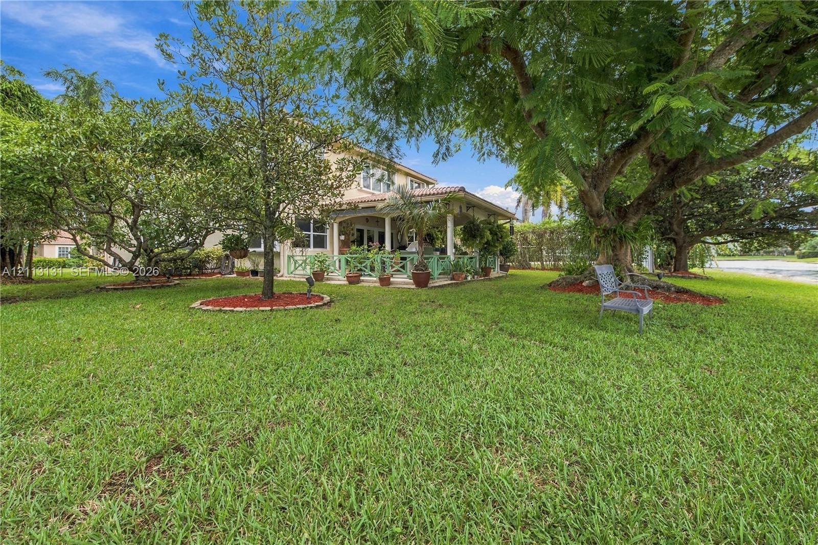 Expansive backyard featuring a sprawling lawn, mature trees, tiered landscape beds with mulch, and a covered patio area with railing