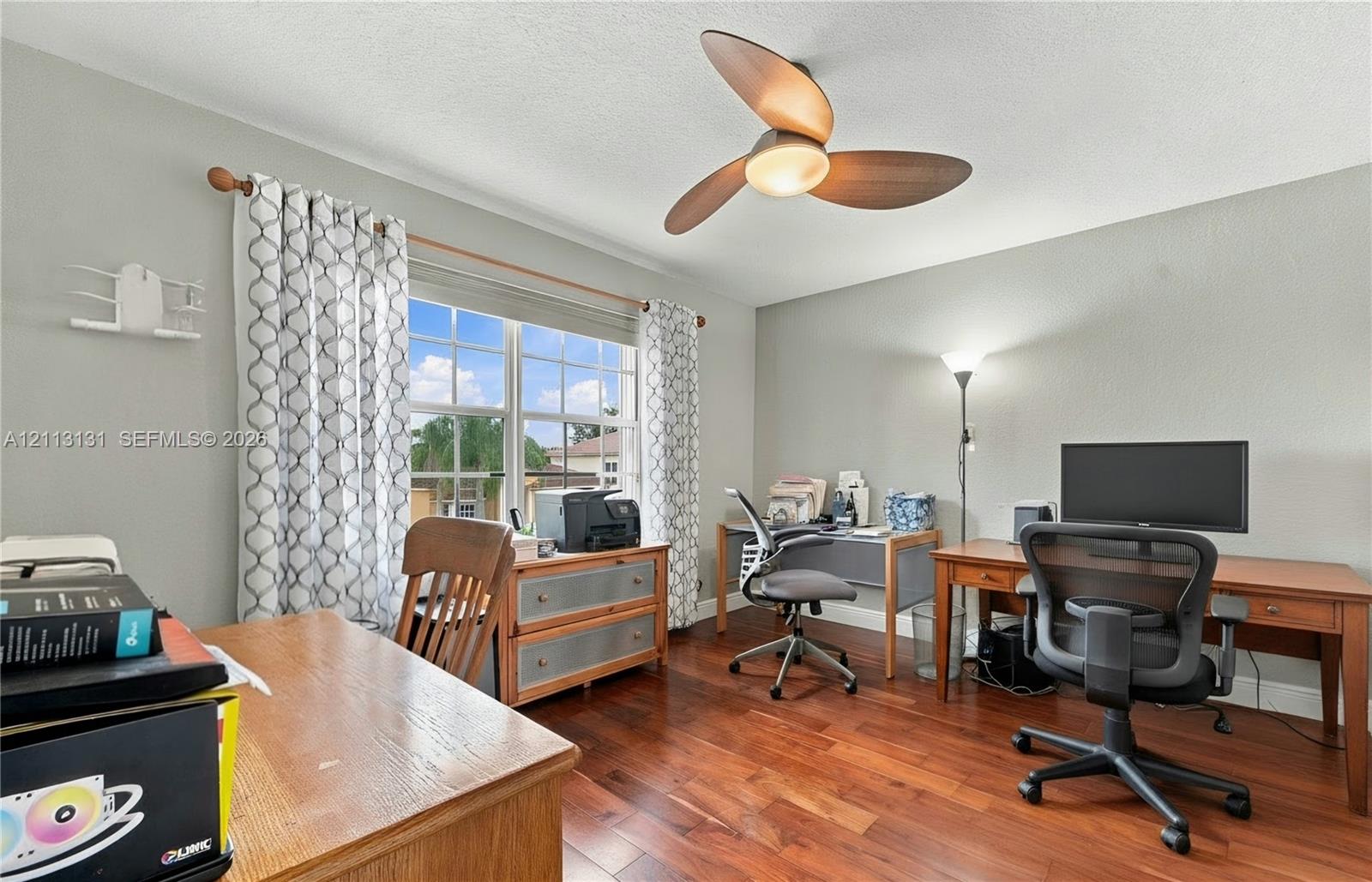 Room featuring wood-finish flooring, a multi-pane window with a curtain rod, and a three-blade ceiling fan with an integrated light fixture