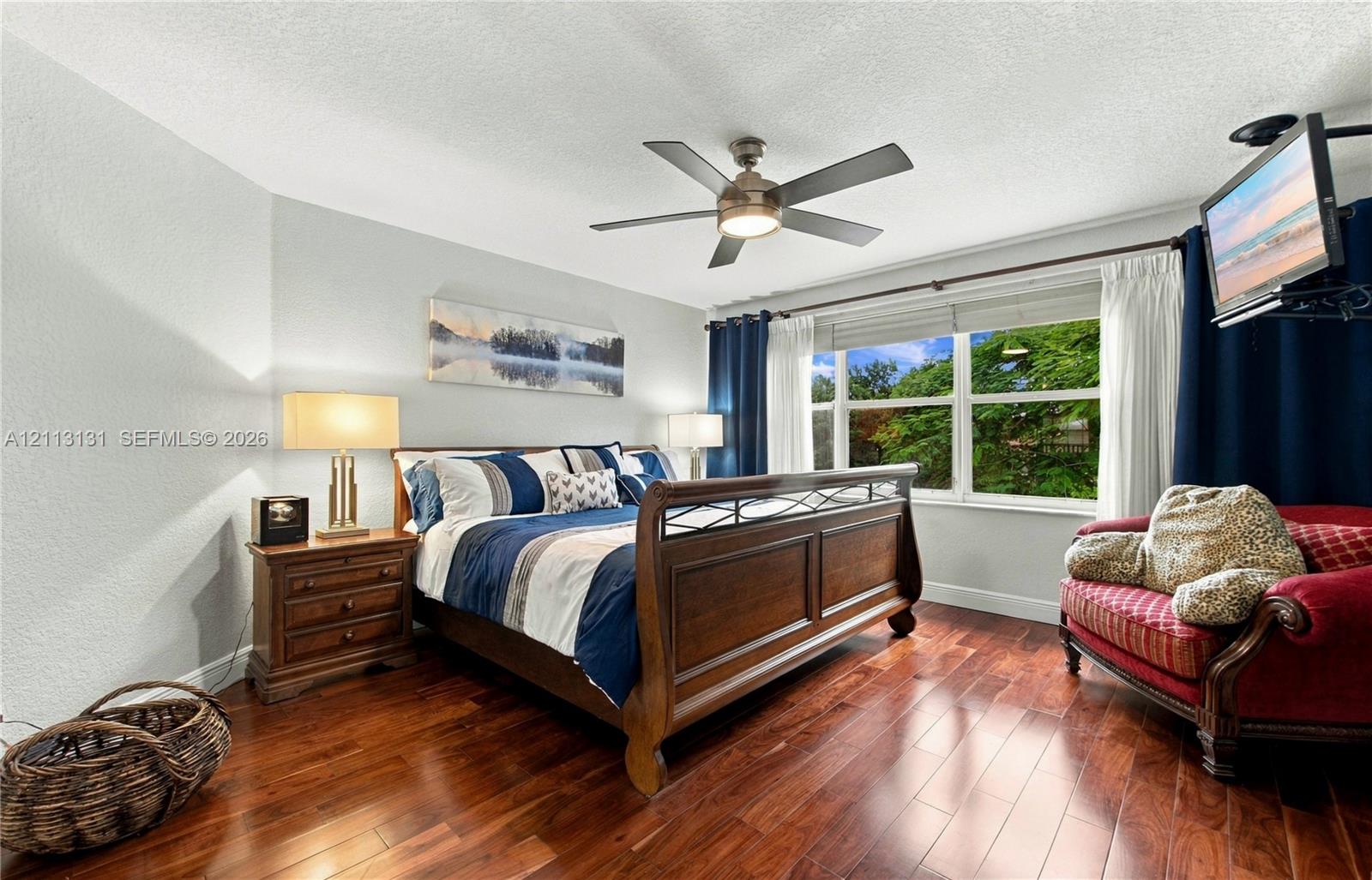 Room featuring wood-finish flooring, a multi-blade ceiling fan with integrated lighting, and a window with natural exterior exposure