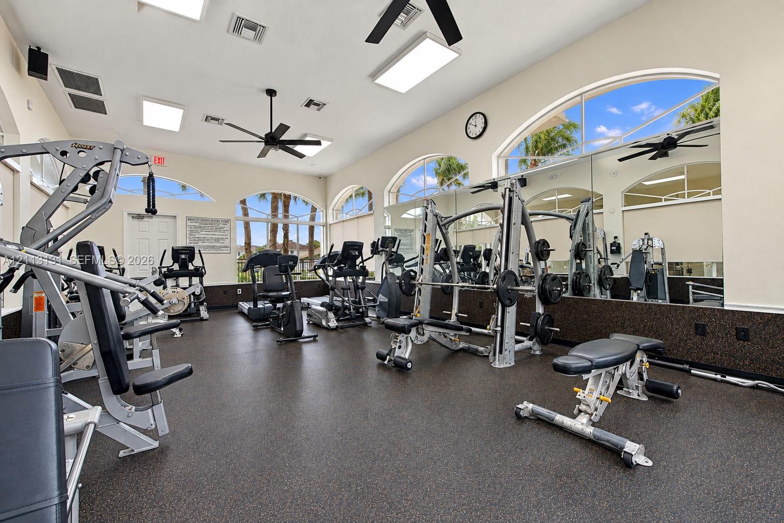 Fitness center featuring rubberized flooring, mirrored walls, arched windows, recessed lighting, and ceiling fans
