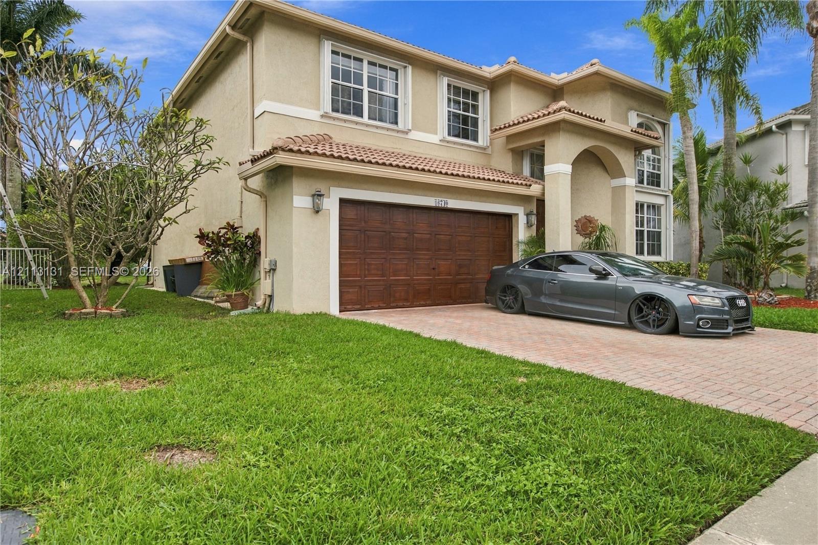 Stucco exterior featuring a dual-pitch tile roof, paver driveway, and a wood-finish two-car garage door