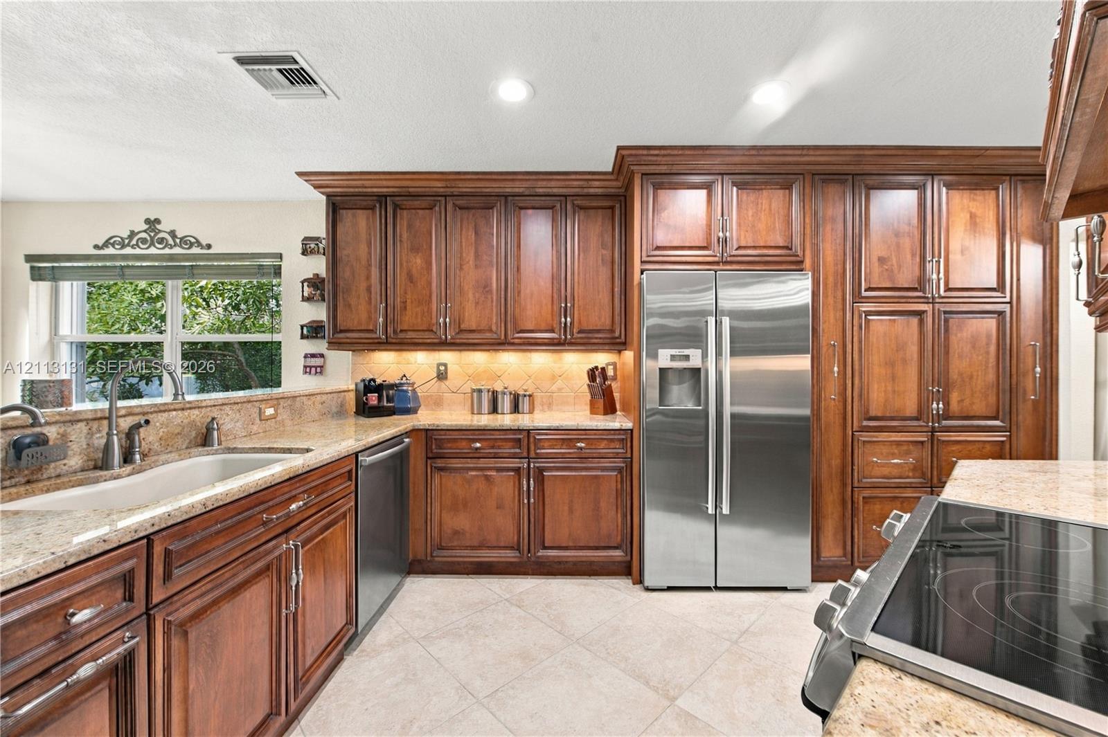 Kitchen featuring stained wood cabinetry, stone countertops, tile flooring, stainless steel side-by-side refrigerator, and built-in electric cooktop