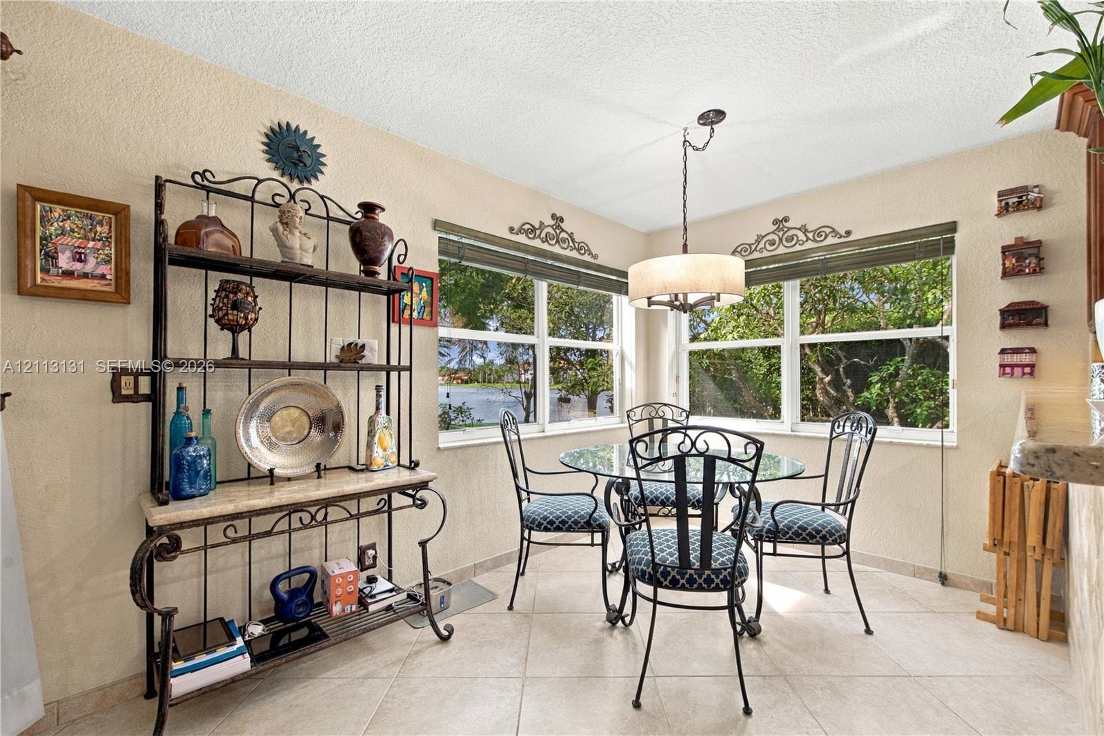 Corner dining area featuring large windows with exterior water scenery, neutral tile flooring, and an overhead drum-style pendant light fixture