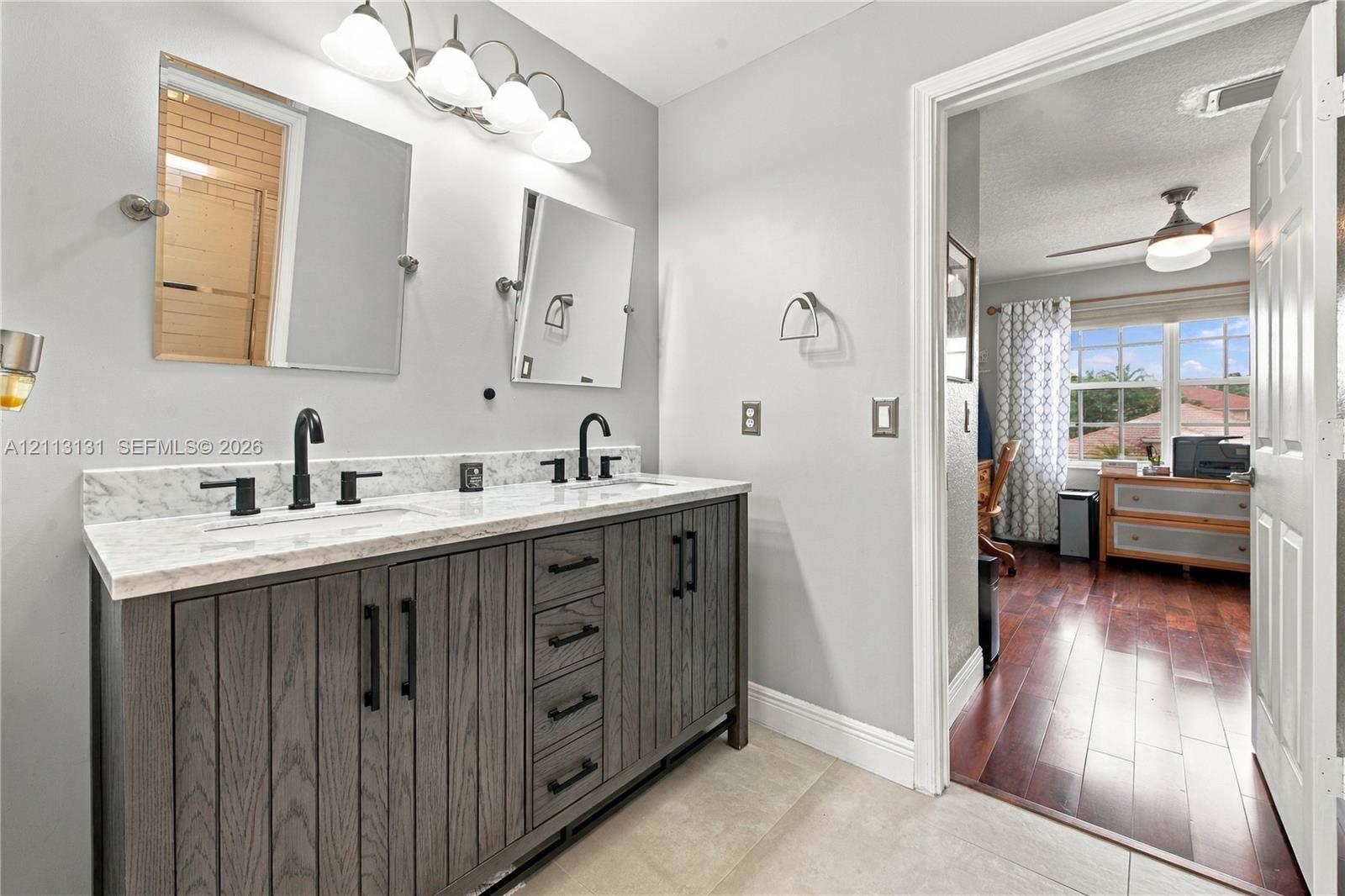 Bathroom featuring a dual-sink vanity with dark wood-finish cabinetry, stone countertop, matte black fixtures, and dual tilting mirrors