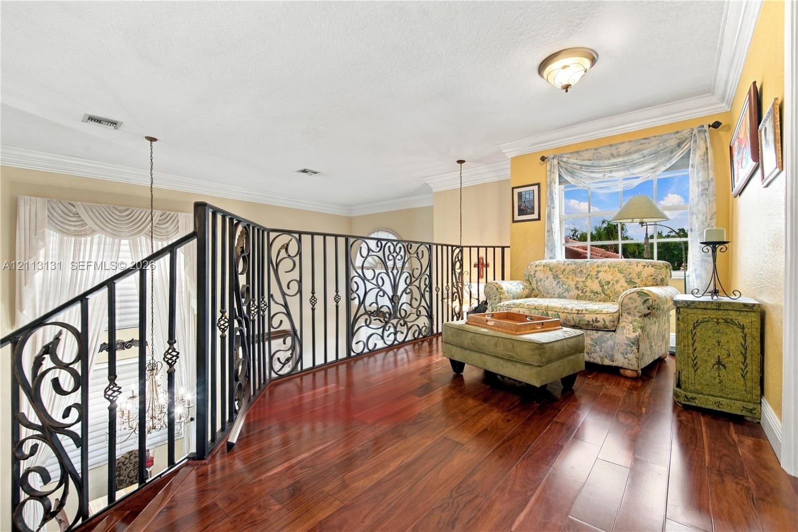 Landing featuring decorative wrought-iron railings, wood-finish flooring, crown molding, and a multi-pane window