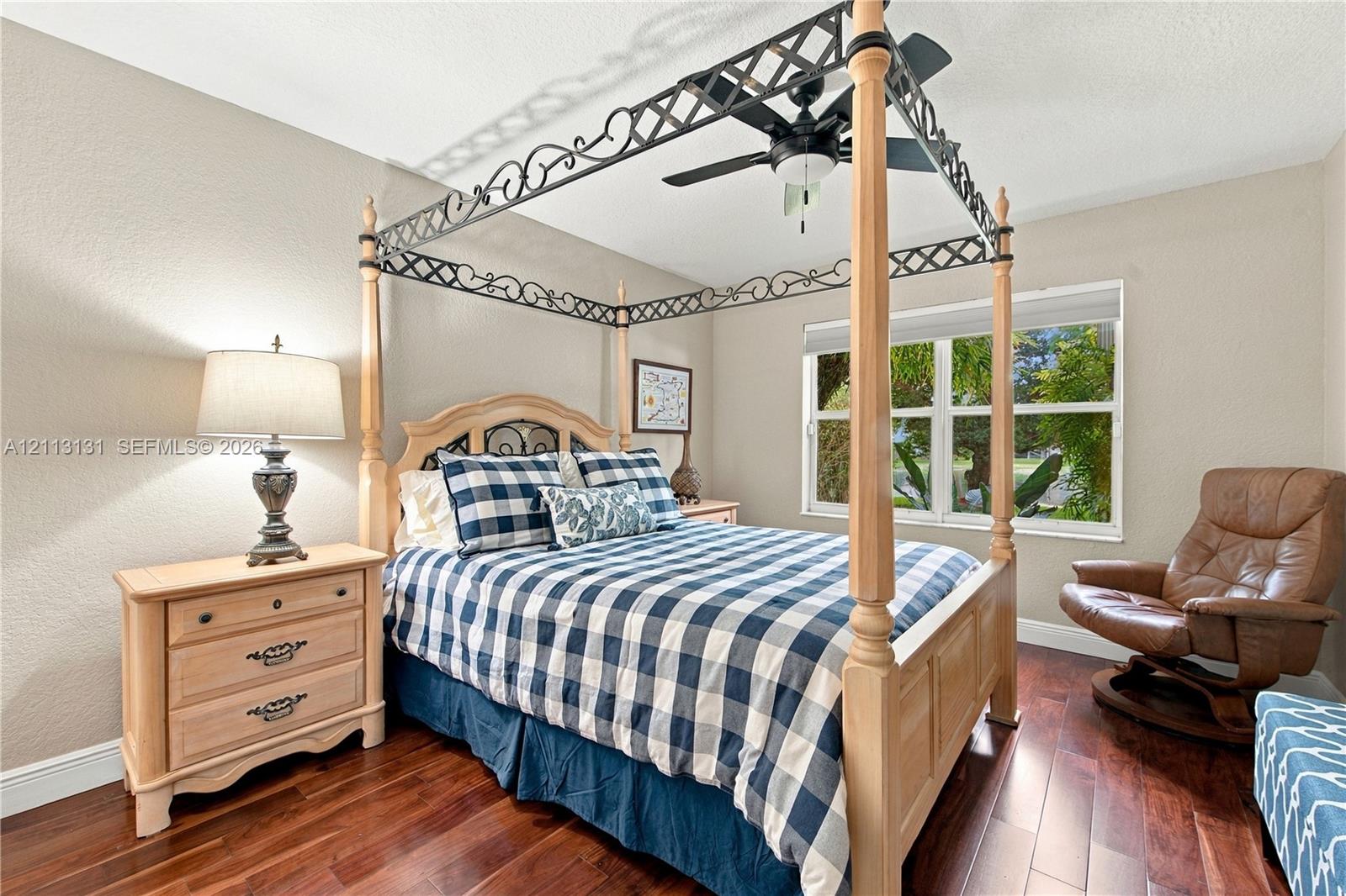 Bedroom featuring dark wood-finish flooring, a multi-pane window, and a ceiling fan with integrated lighting