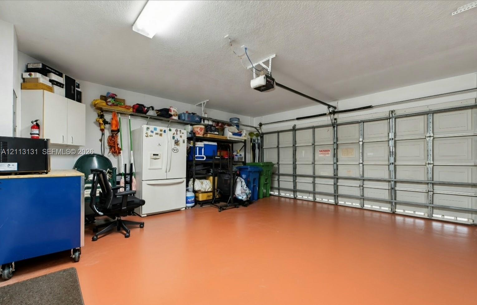 Two-car garage featuring a painted concrete floor, white wall-mounted cabinetry, an automated garage door opener, and overhead lighting