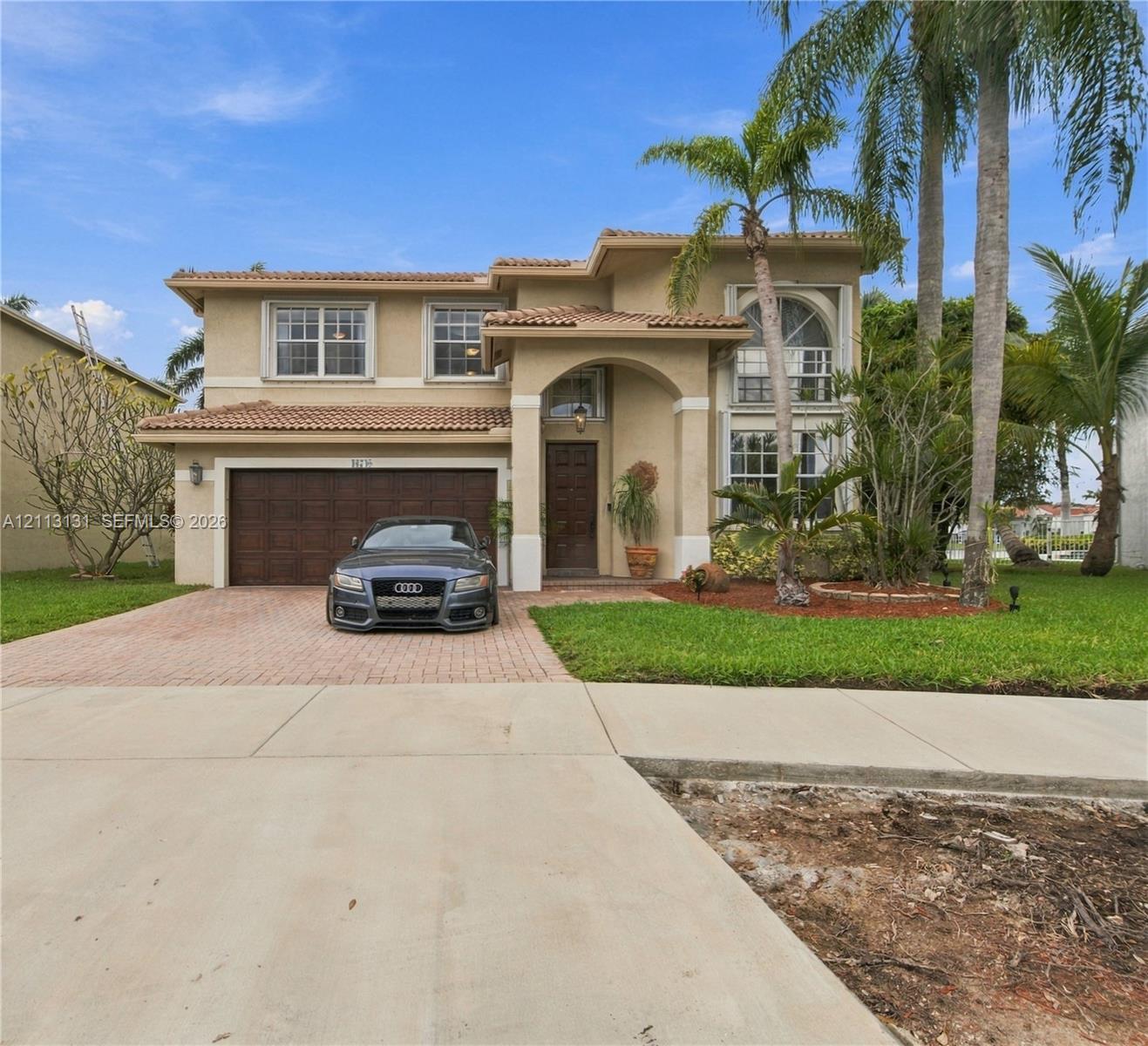 Two-story stucco exterior featuring a clay tile roof, arched entryway, multi-paned windows, and a paver driveway