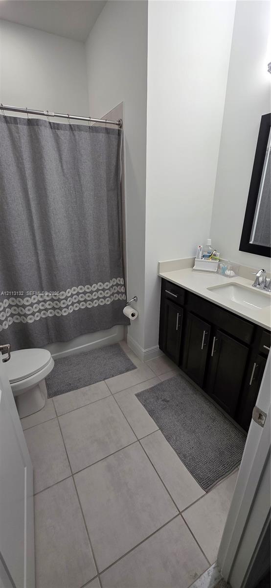 Bathroom featuring dark wood-finish cabinetry, a light-toned solid surface countertop, rectangular under-mount sink, tiled flooring, and a shower-tub combination