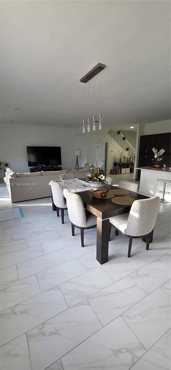 Large-format tile flooring with a neutral veined finish, multi-light linear pendant fixture, and white cabinetry