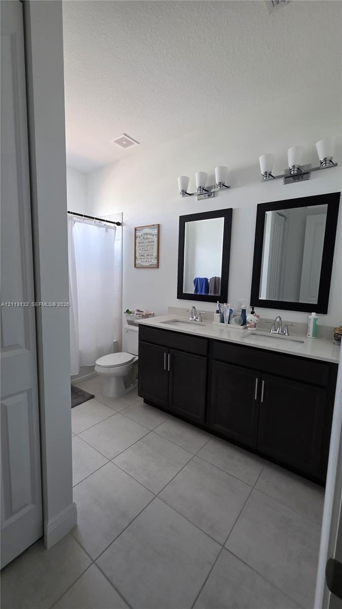 Double vanity with dark cabinetry, stone-finish countertops, dual framed mirrors, and large-format neutral tile flooring