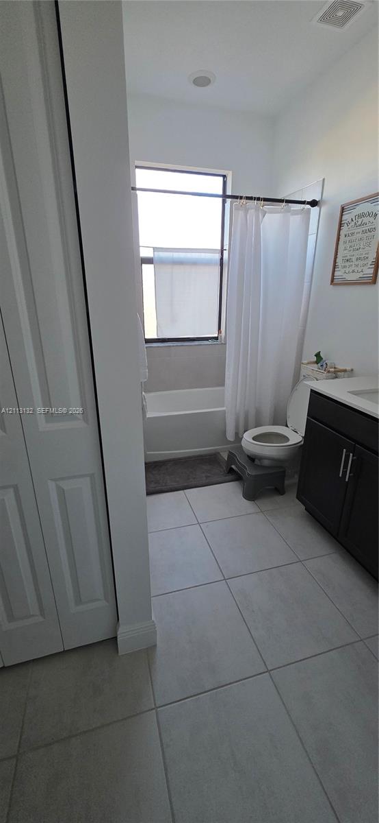 Bathroom featuring large-format tile flooring, vanity with dark-finish cabinetry, countertop with integrated sink, and a combination bathtub and shower enclosure with a window