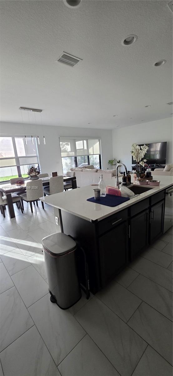 Kitchen featuring a center island with a stone countertop, dark cabinetry, recessed ceiling lighting, and tile flooring throughout