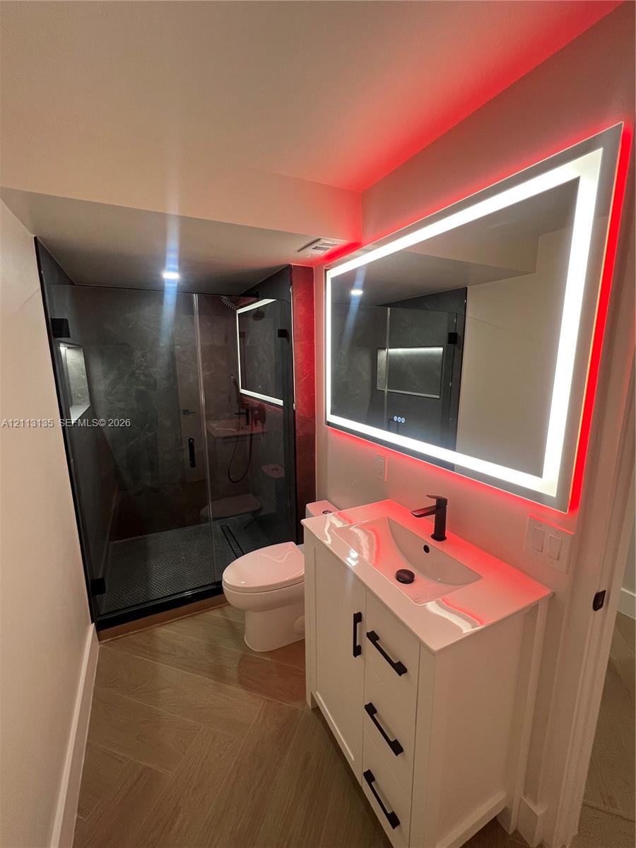 White vanity with matte black hardware, integrated sink, and stone-finish countertop paired with a rectangular LED-backlit mirror