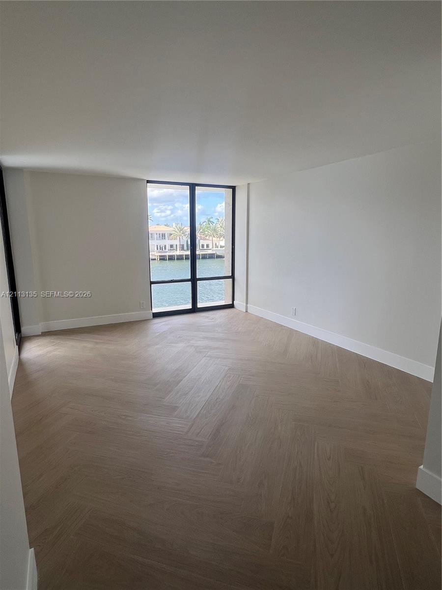 Herringbone wood-finish flooring, floor-to-ceiling windows with black metal frames, and water exposure