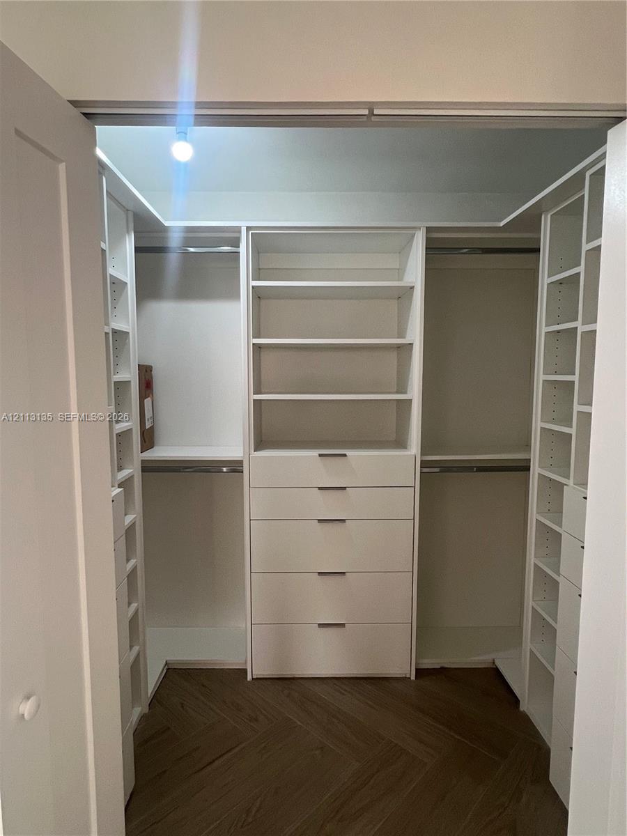 Walk-in closet featuring white built-in shelving, integrated storage drawers, hanging rods, and herringbone-patterned wood-finish flooring