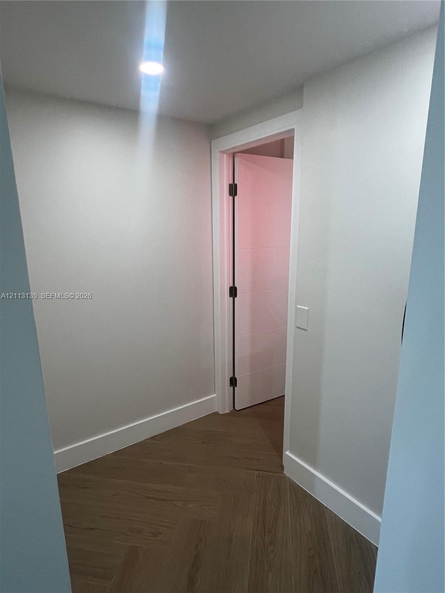 Herringbone-patterned wood-finish flooring, recessed ceiling lighting, and a solid-core interior door with matte black hardware